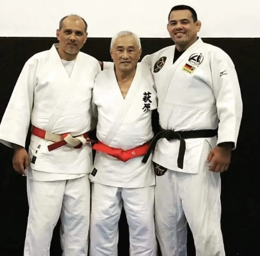 Três judocas de quimono branco lado a lado; o do centro usa faixa vermelha e traz o sobrenome Haguihara em kanji no quimono.